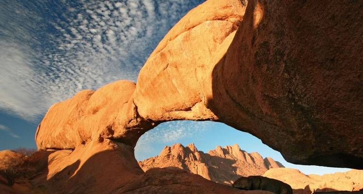 Natural rock arch formation with mountains in the background.