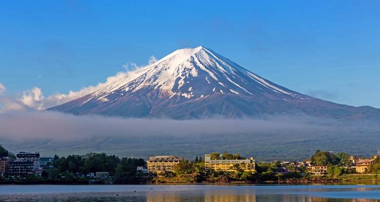 Mount Fuji with a town in the foreground and a lake reflecting the image.