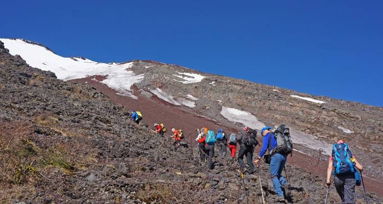 A group of hikers climbing a rocky mountain trail with snow patches.