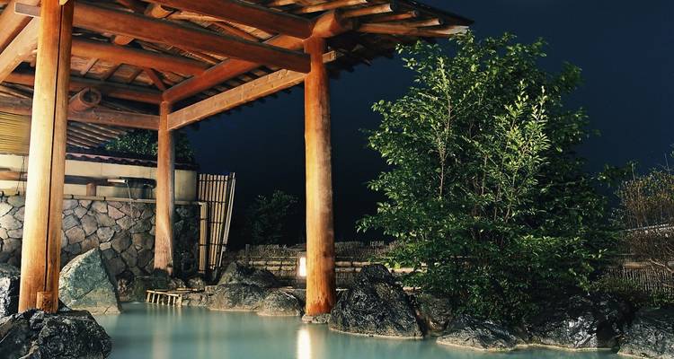 An onsen or hot spring surrounded by rocks and illuminated at night.