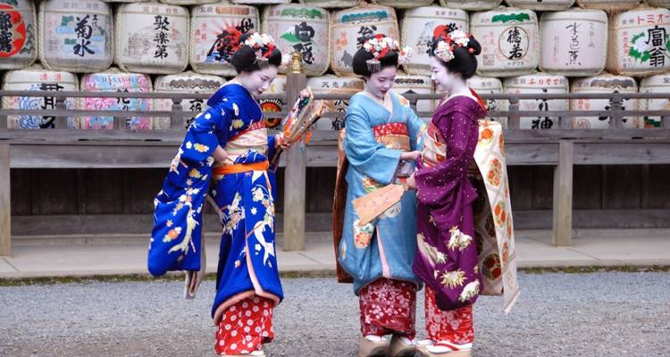 Three geishas dressed in traditional kimono standing together, smiling.