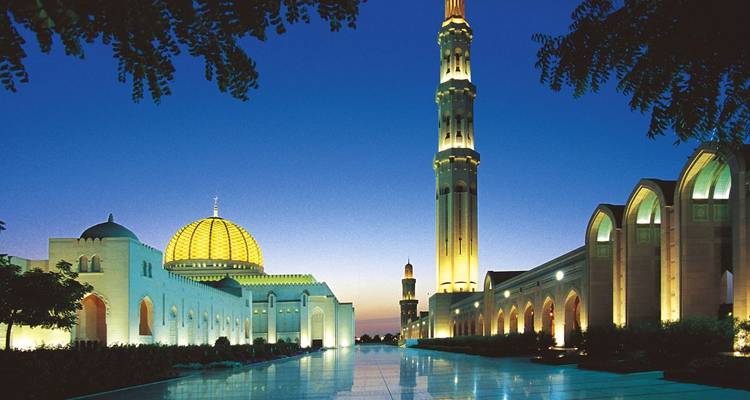 Grand mosque with illuminated domes and minarets during twilight.