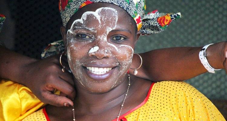 Woman with traditional face paint and colorful headscarf smiling.
