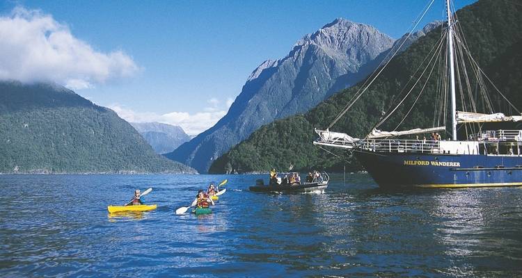 Des gens faisant du kayak et de la navigation de plaisance avec un décor de montagnes pittoresques en arrière-plan.