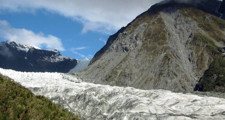 Un glacier avec des montagnes escarpées en arrière-plan sous un ciel bleu avec quelques nuages.