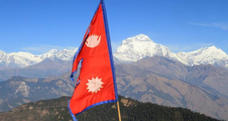Nepalese nationale vlag wapperend tegen een achtergrond van besneeuwde Annapurna bergketen gezien vanaf een hoge bergkam.