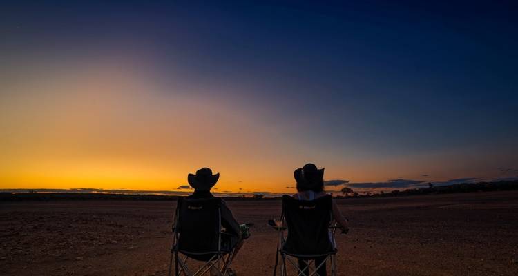 Deux personnes assises sur des chaises regardant un coucher de soleil coloré.