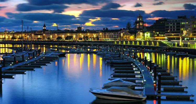 Harbor with boats reflecting city lights at dusk.