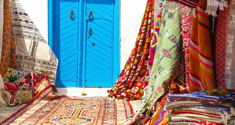 Colorful rugs displayed outside a blue door.