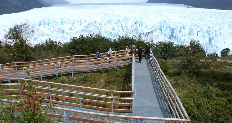 Des touristes marchant sur une promenade en bois avec vue sur un glacier.