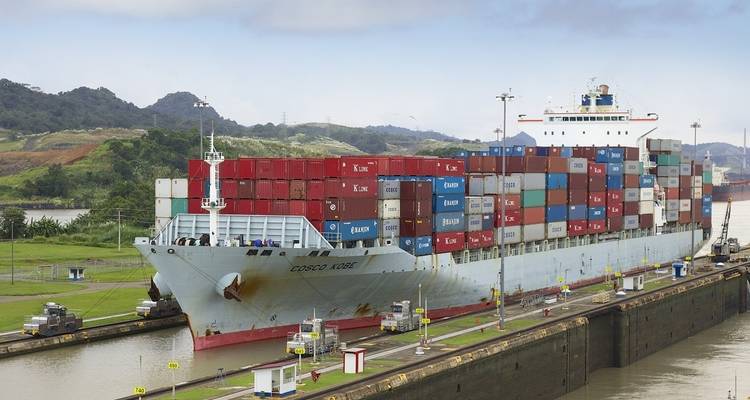 Ein großes Frachtschiff voller bunter Container, das durch einen Kanal navigiert.