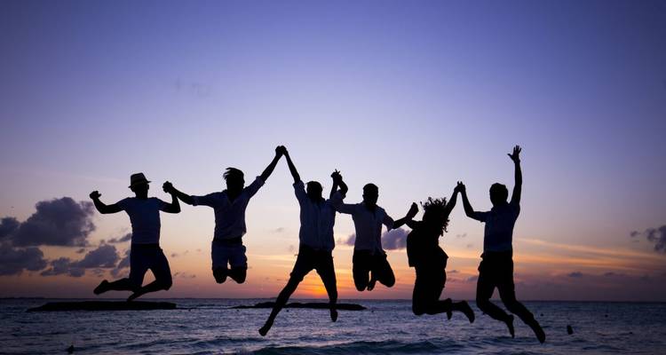 Silhouette von Menschen, die bei Sonnenuntergang am Strand springen.