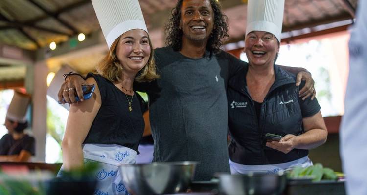 Three smiling people wearing chef hats in a cooking class.