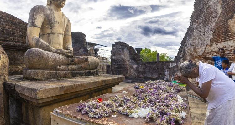 A person praying at a Buddhist site with flowers.