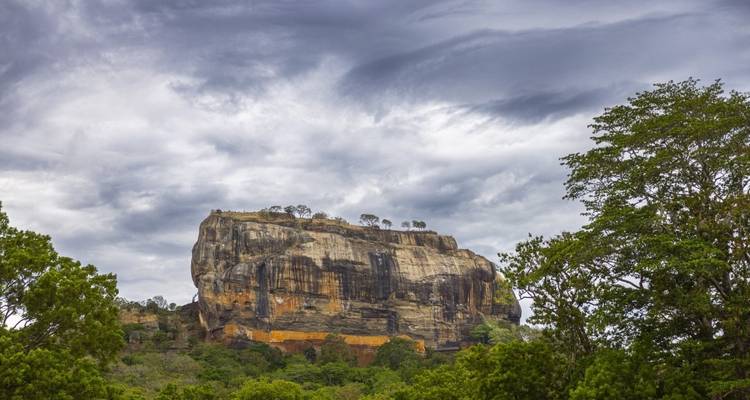 A large rock formation in a lush landscape under an overcast sky.