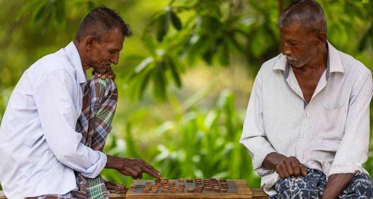 Two elderly men playing a board game outdoors.