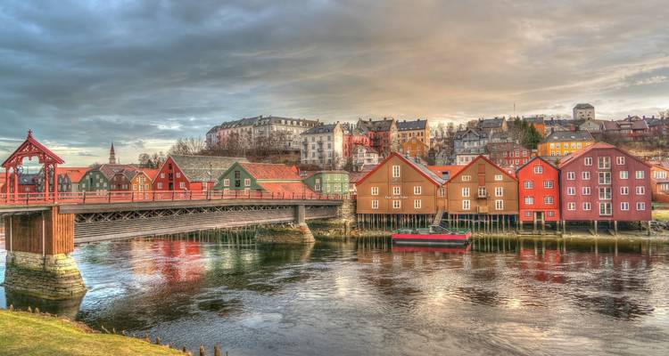View of colorful buildings lining a riverside with a unique bridge.