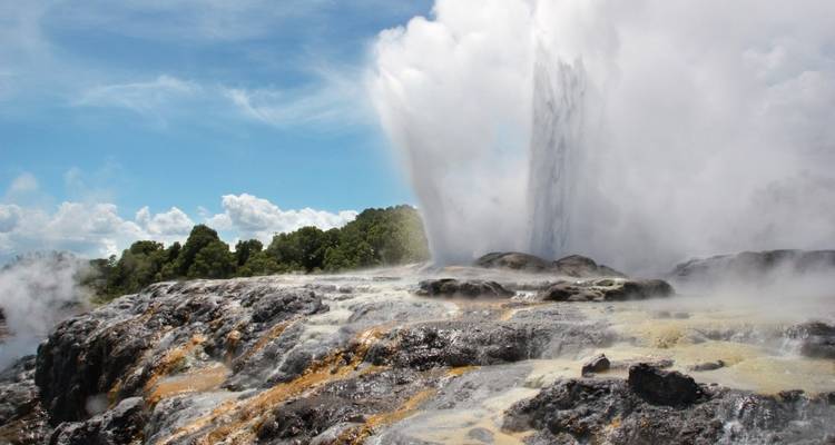 Geyser erupting with steam against a blue sky.