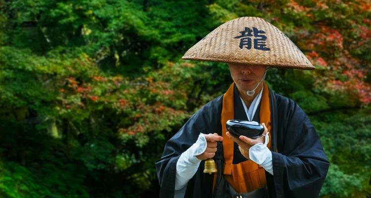 Persona con vestimenta tradicional japonesa con una campana en un jardín