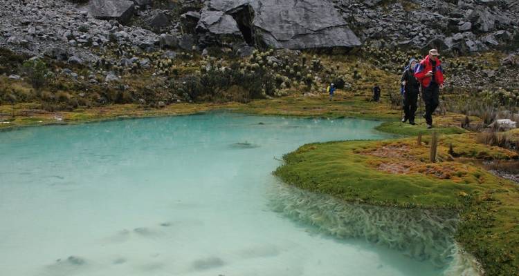 Excursionistas junto a un estanque azul cristalino en terreno montañoso.