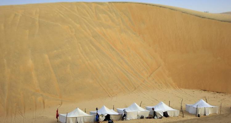 Zelte aufgeschlagen am Fuß einer großen Sanddüne in einer Wüste.