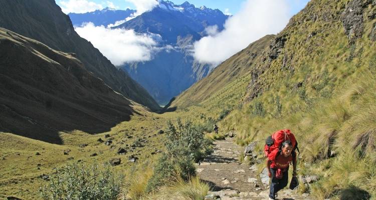 Person hiking on a steep trail with mountains in the background.