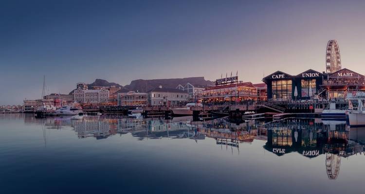 Waterfront with ferris wheel and tabletop mountain at night.