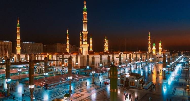 Illuminated grand mosque at night with bright lights.