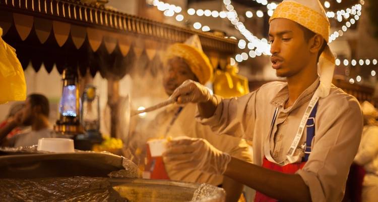 Street food vendor serving in a lit-up market area.