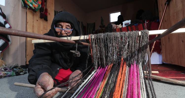 Elderly woman working on colorful textile weaving.