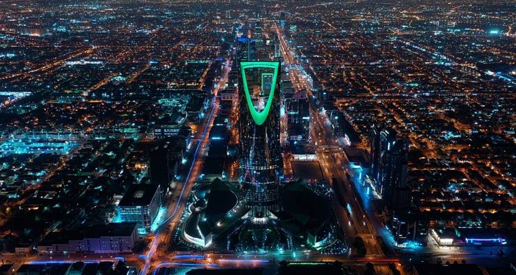 Aerial view of a bustling cityscape at night with a lit-up tower.