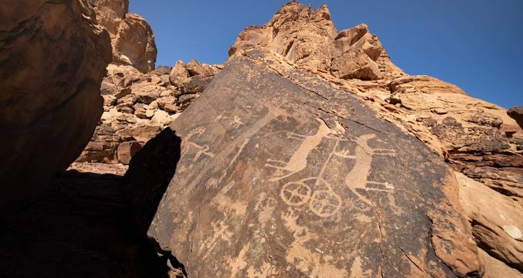 Petroglyphs on a large rock under a bright blue sky.