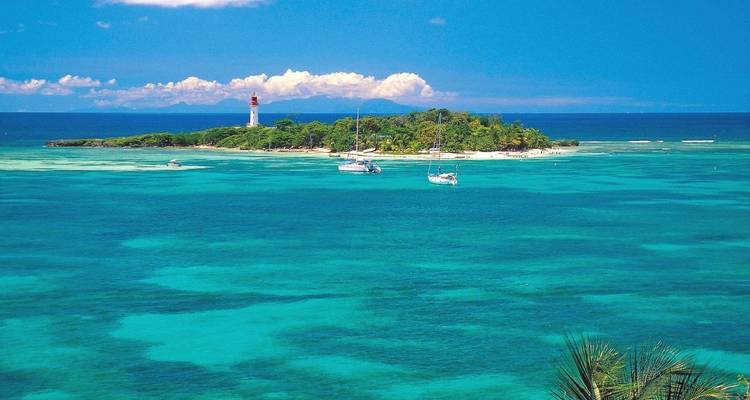 Isla tropical con un faro, rodeada de agua turquesa y veleros.