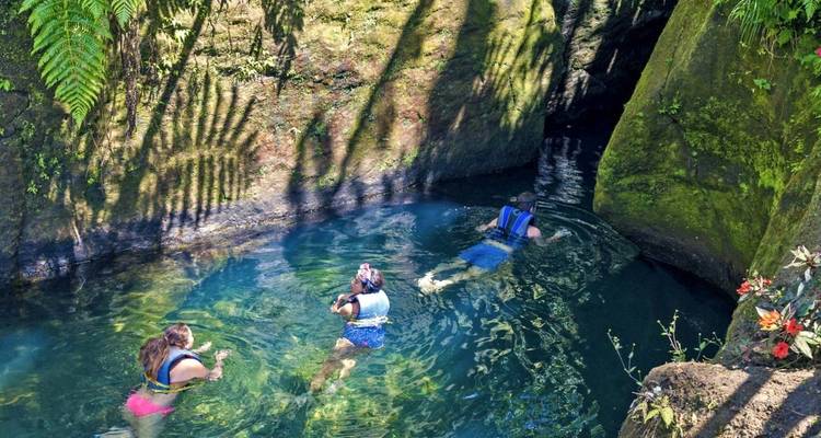 Personas haciendo snorkel en una piscina natural cristalina rodeada de vegetación exuberante.