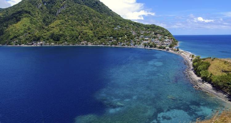 Pueblo costero enclavado entre una colina verde y una bahía azul vibrante.