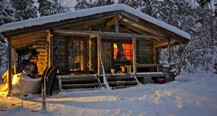 Chalet en rondins douillet dans un paysage hivernal enneigé avec un éclairage chaleureux.