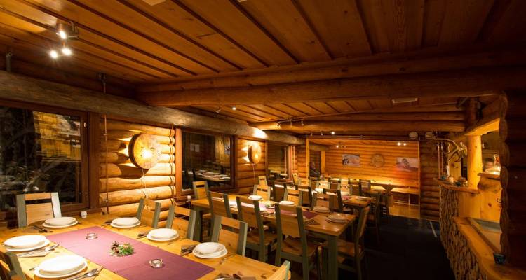 Salle à manger chaleureusement éclairée avec de longues tables en bois et des murs en rondins préparée pour un repas de groupe