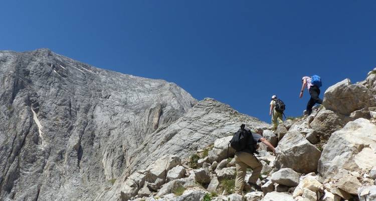 Hikers ascending a rocky mountain path with a clear sky.