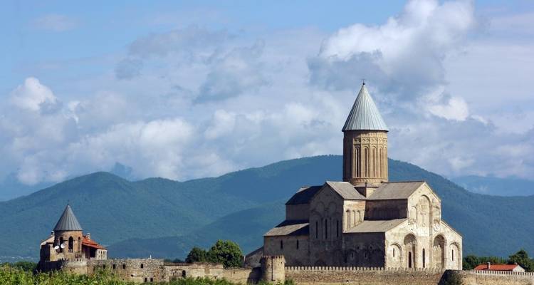 Catedral de Svetitskhoveli situada contra un telón de fondo de montañas y cielo azul.