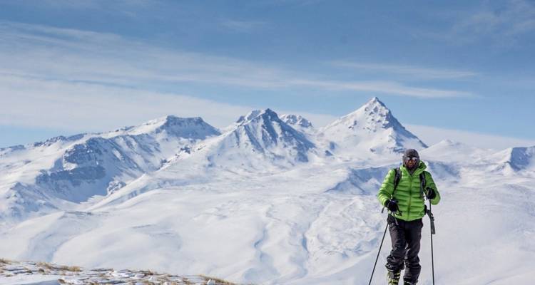 Esquiador en una llanura nevada con un dramático telón de fondo montañoso.
