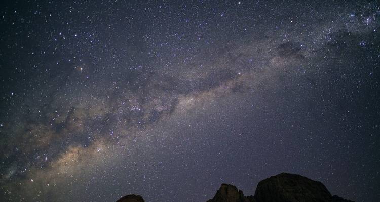 Cielo nocturno estrellado con la Vía Láctea sobre siluetas oscuras de montañas.