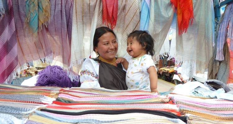 Una mujer y un niño sonriendo en un mercado textil vibrante.