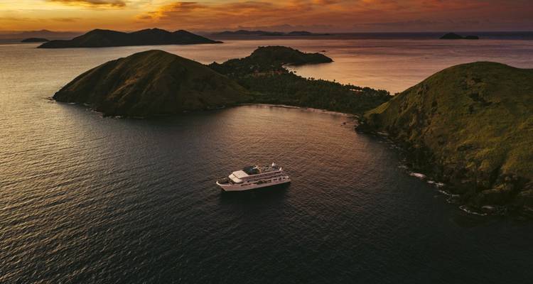 Navire de croisière naviguant près des îles au coucher du soleil.