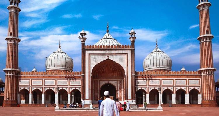Person in traditioneller Kleidung, die vor einer großen Moschee steht.