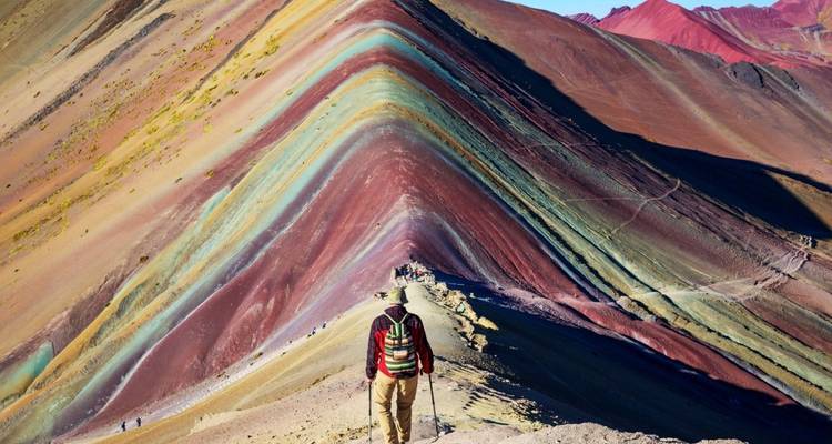 Colorful layers of mountains known as Rainbow Mountain with a hiker in the foreground.