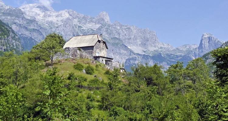 A stone building with mountainous backdrop surrounded by lush greenery.