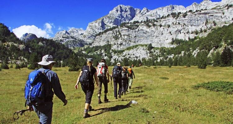 A group of hikers walking through a grassy valley with mountainous background.