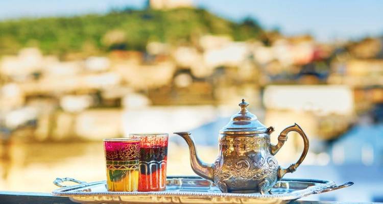 Silberne Teekanne und Gläser auf einem Tablett mit unscharfer Stadtsilhouette.