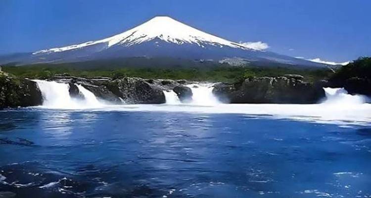 Río azul impetuoso y cascadas enmarcadas por el volcán Osorno con su cumbre blanca como la nieve.