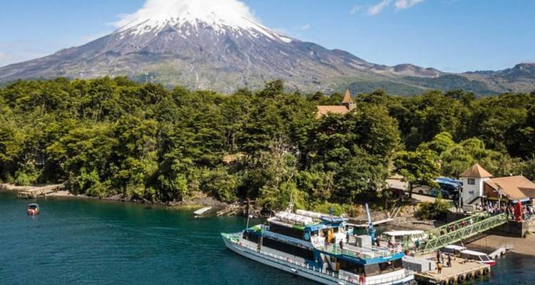 Bote de tours atracado en un lago azul profundo rodeado de bosque con el volcán Osorno elevándose detrás.